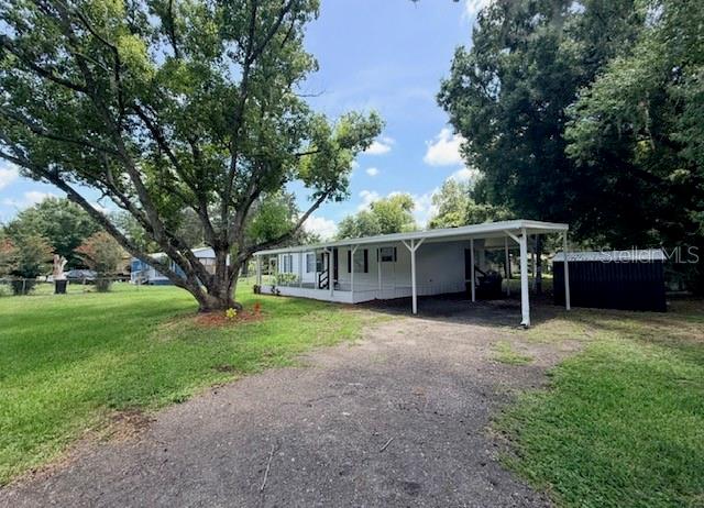 A single-story mobile home with a carport and a large tree in the front yard — 4394 RAMBLEWOOD N, MULBERRY, FL
