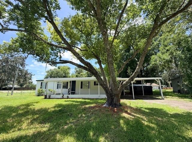 A white manufactured home with a screened porch and carport sits behind a large tree — 4394 RAMBLEWOOD N, MULBERRY, FL