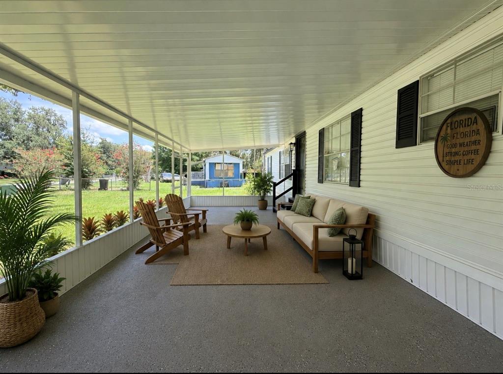 A screened-in porch features a beige sofa, two wooden chairs, a coffee table, and plants — 4394 RAMBLEWOOD N, MULBERRY, FL