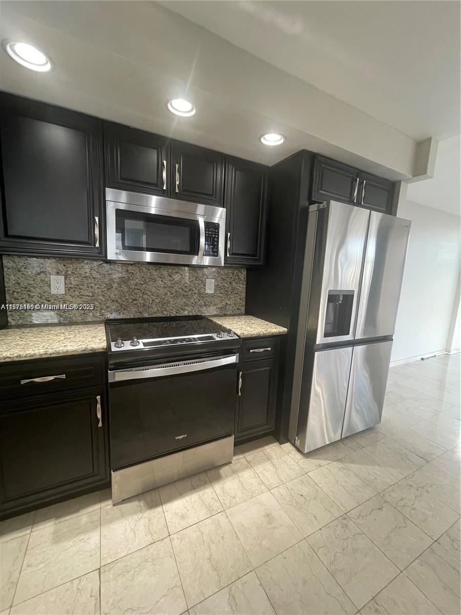 A kitchen features dark cabinetry, stainless steel appliances, and granite countertops over tile flooring — 1000 Parkview Dr # 920, Hallandale Beach FL 33009, HALLANDALE BEACH, FL