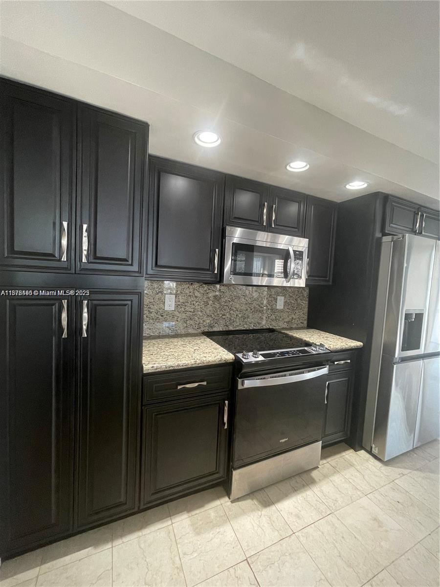 A kitchen features dark wood cabinets, granite countertops, and stainless steel appliances — 1000 Parkview Dr # 920, Hallandale Beach FL 33009, HALLANDALE BEACH, FL