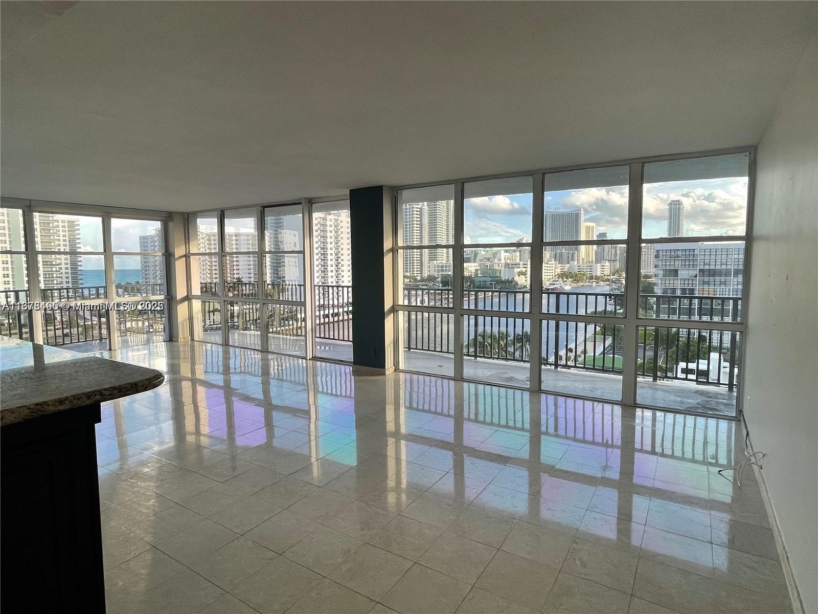 An empty room with light-colored tile floors and floor-to-ceiling windows overlooking a city waterfront — 1000 Parkview Dr # 920, Hallandale Beach FL 33009, HALLANDALE BEACH, FL