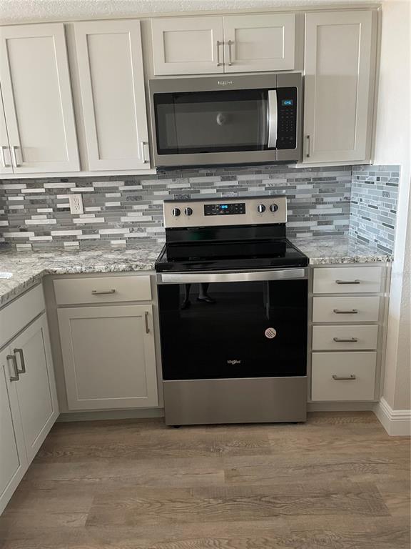 A kitchen features light gray cabinets, stainless steel appliances, granite countertops, and a mosaic backsplash — 6177 SUN BOULEVARD UNIT 405, ST PETERSBURG, FL