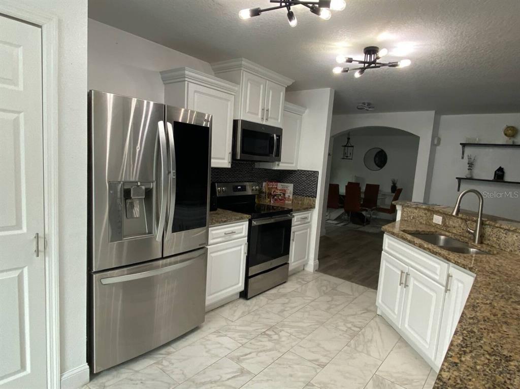 A kitchen features white cabinets, stainless steel appliances, granite countertops, and light-colored tile flooring — 660 SWALLOWTAIL DRIVE, HAINES CITY, FL