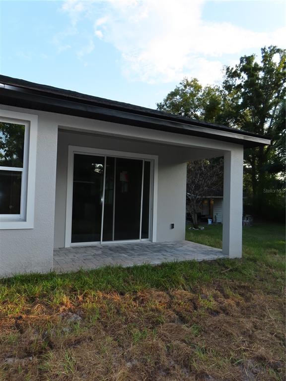 A covered concrete patio with a sliding glass door sits beside a gray stucco house — 4525 RALEIGH STREET, ORLANDO, FL