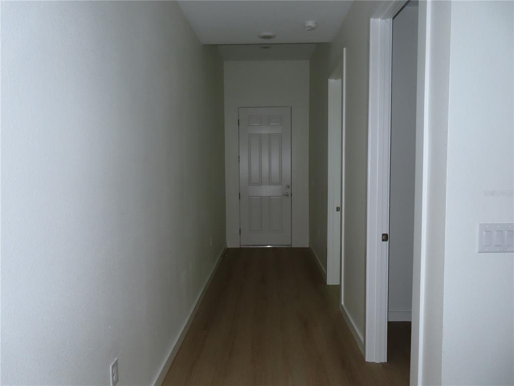 A hallway with light wood-look flooring leads to a white door at the end — 4525 RALEIGH STREET, ORLANDO, FL