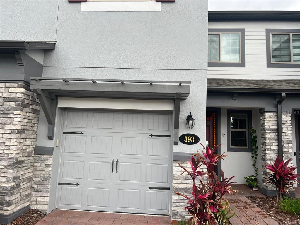 The exterior of a two-story townhouse features a gray garage door, stone accents, and landscaping — 393 EVERTREE LOOP, SANFORD, FL
