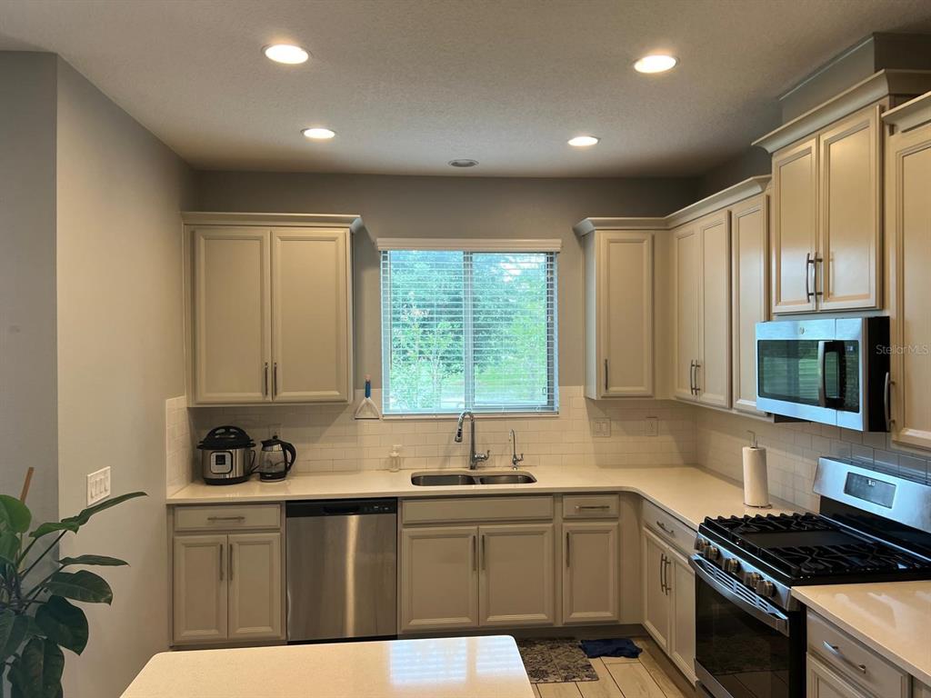 A kitchen featuring light-colored cabinets, stainless steel appliances, a white subway tile backsplash, and countertops — 393 EVERTREE LOOP, SANFORD, FL