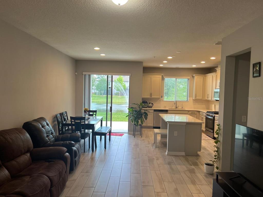 An open-concept kitchen and living area features tile flooring, light cabinetry, and a sliding door — 393 EVERTREE LOOP, SANFORD, FL