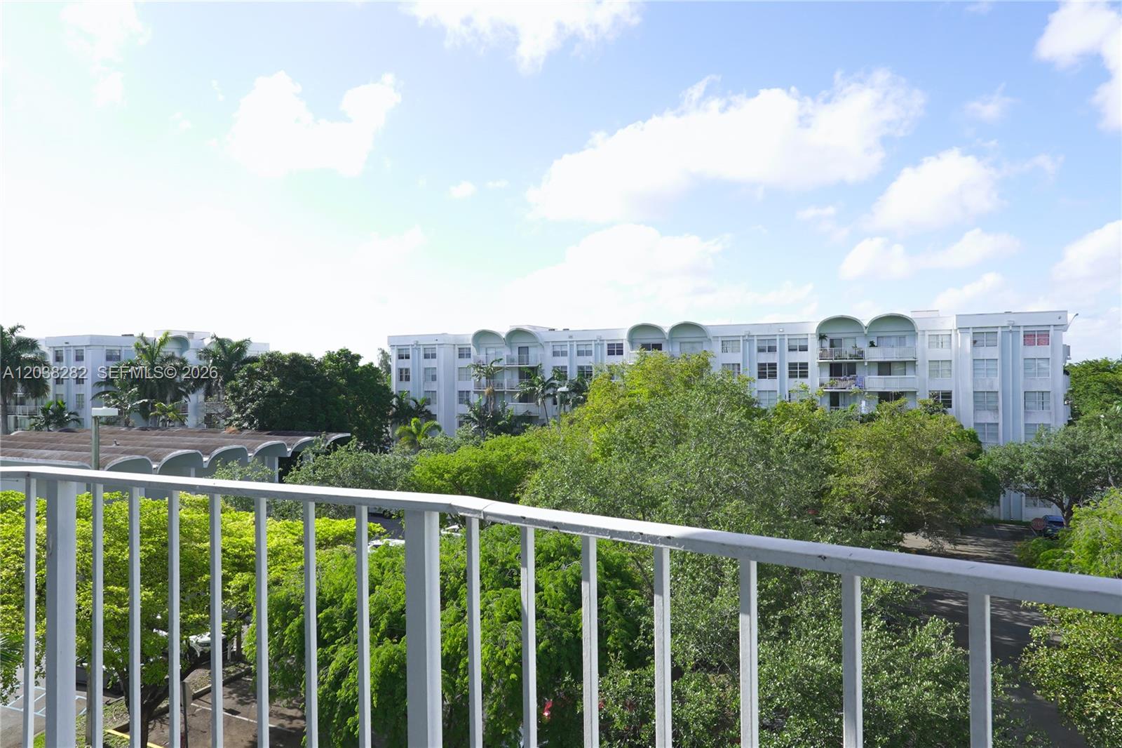 A balcony overlooks lush green trees and multi-story residential apartment buildings under a blue sky — 482 NW 165th St Rd # A504, Miami FL 33169, MIAMI, FL