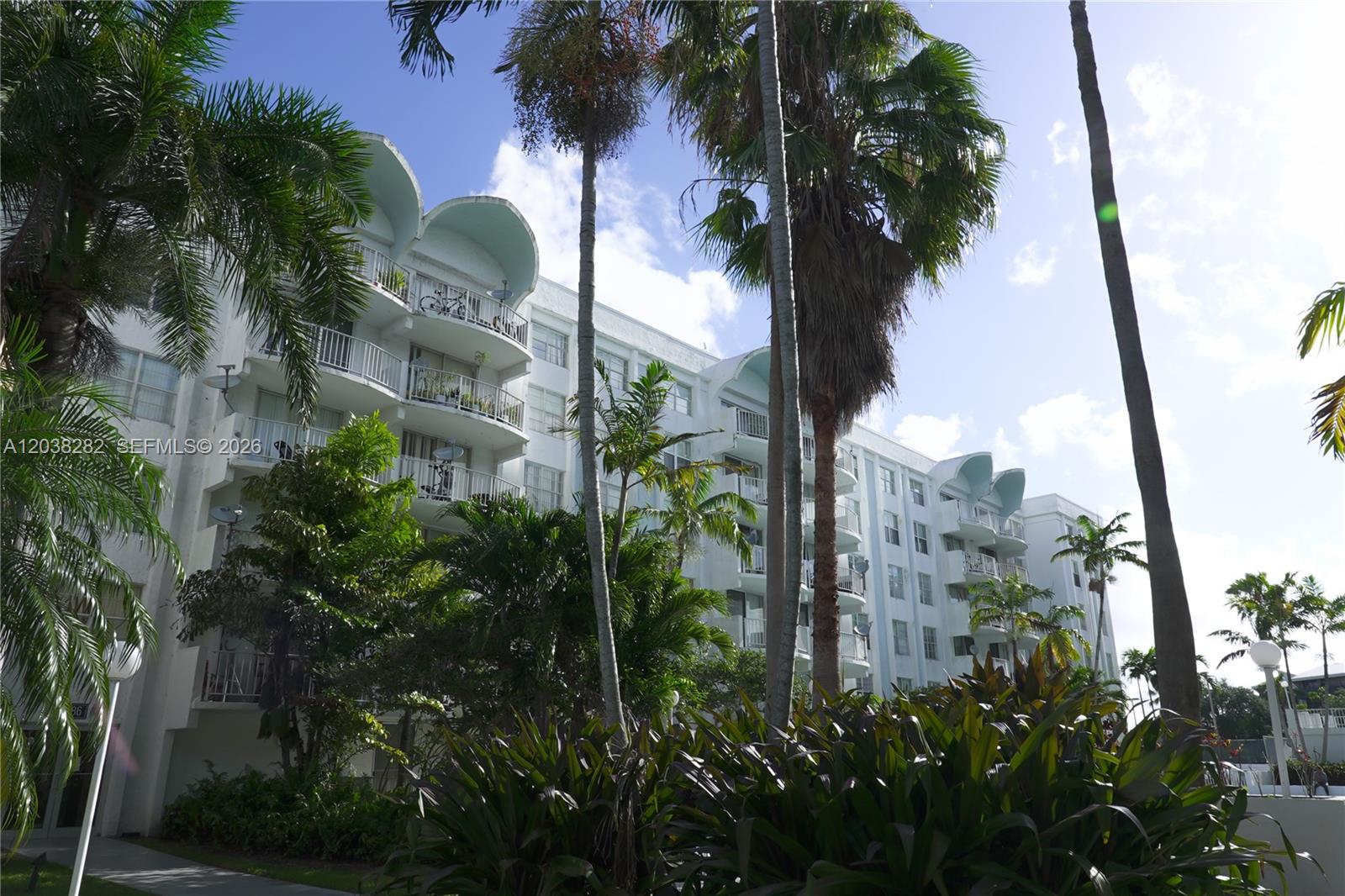 A multi-story white apartment building features curved rooflines and balconies surrounded by palm trees — 482 NW 165th St Rd # A504, Miami FL 33169, MIAMI, FL