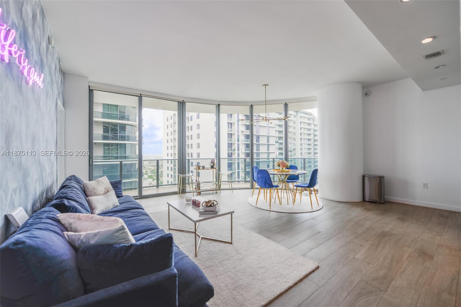 A living and dining area features blue furniture, floor-to-ceiling windows, and light wood flooring — 45 SW 9th ST # 4108, Miami FL 33130, MIAMI, FL