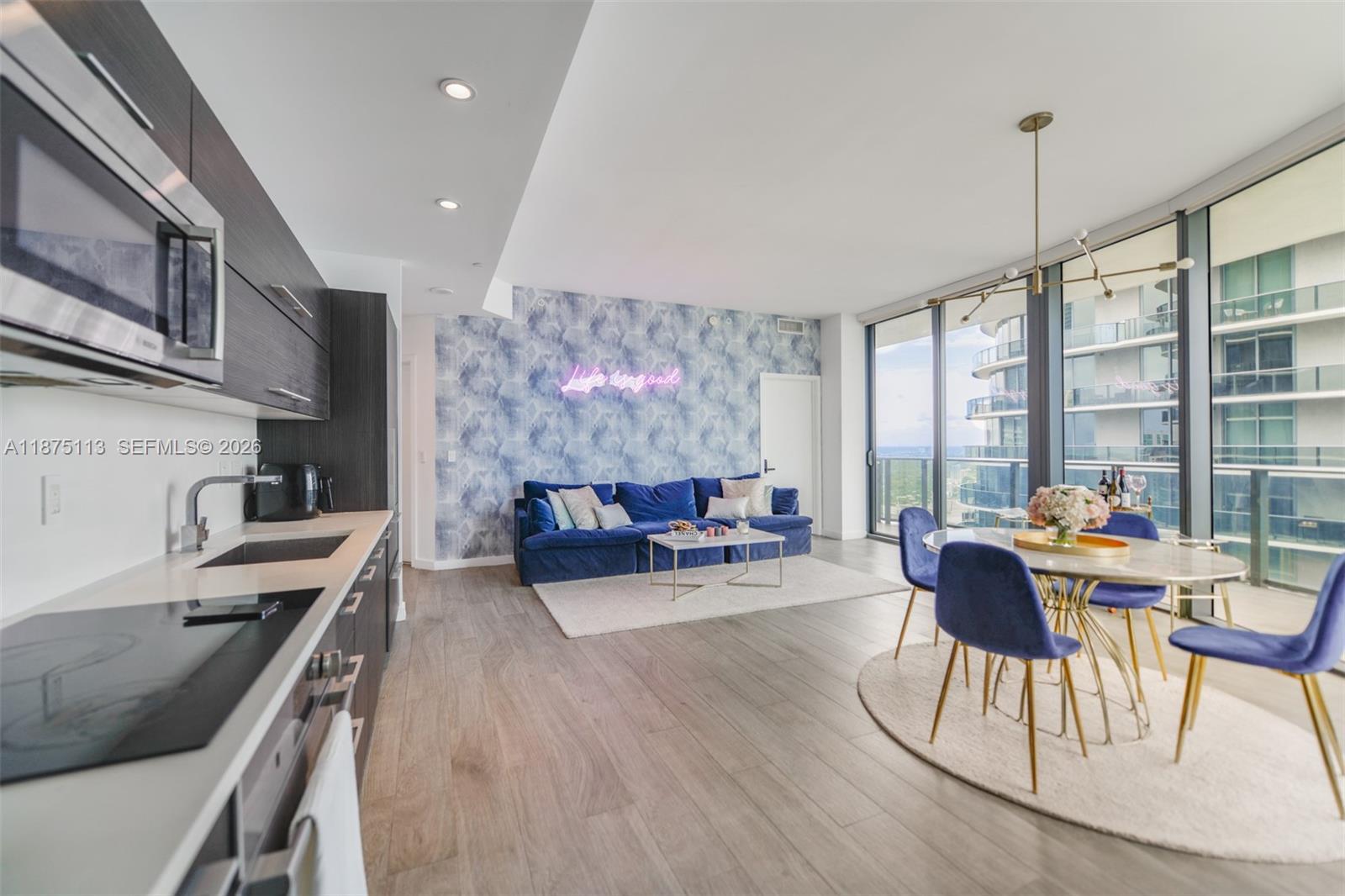 An open-concept living and dining area features a blue sofa, patterned wallpaper, and floor-to-ceiling windows — 45 SW 9th ST # 4108, Miami FL 33130, MIAMI, FL