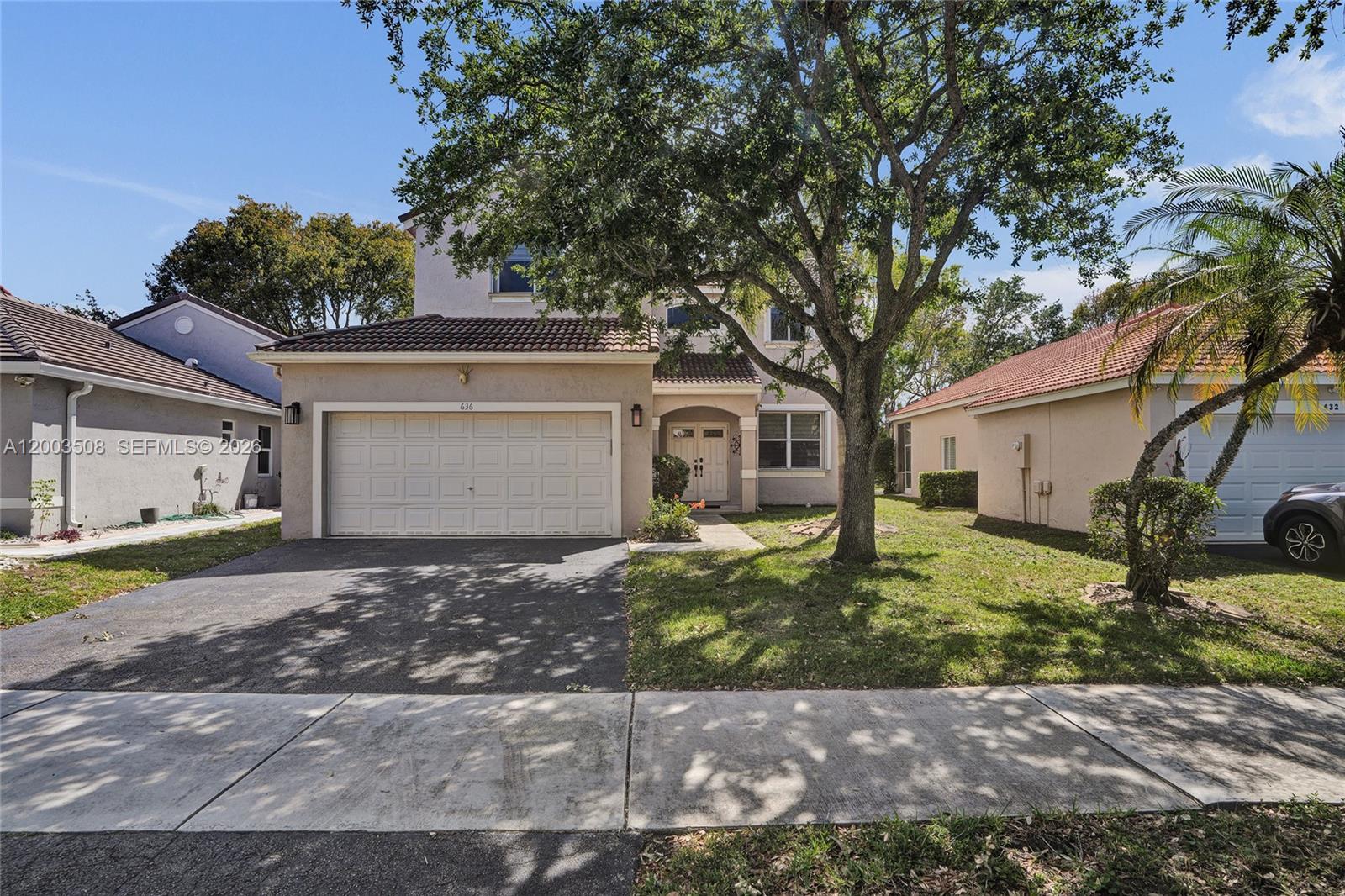 A two-story suburban house with a garage, driveway, and a large tree in the yard — 636 Sand Creek Cir, Weston FL 33327, WESTON, FL