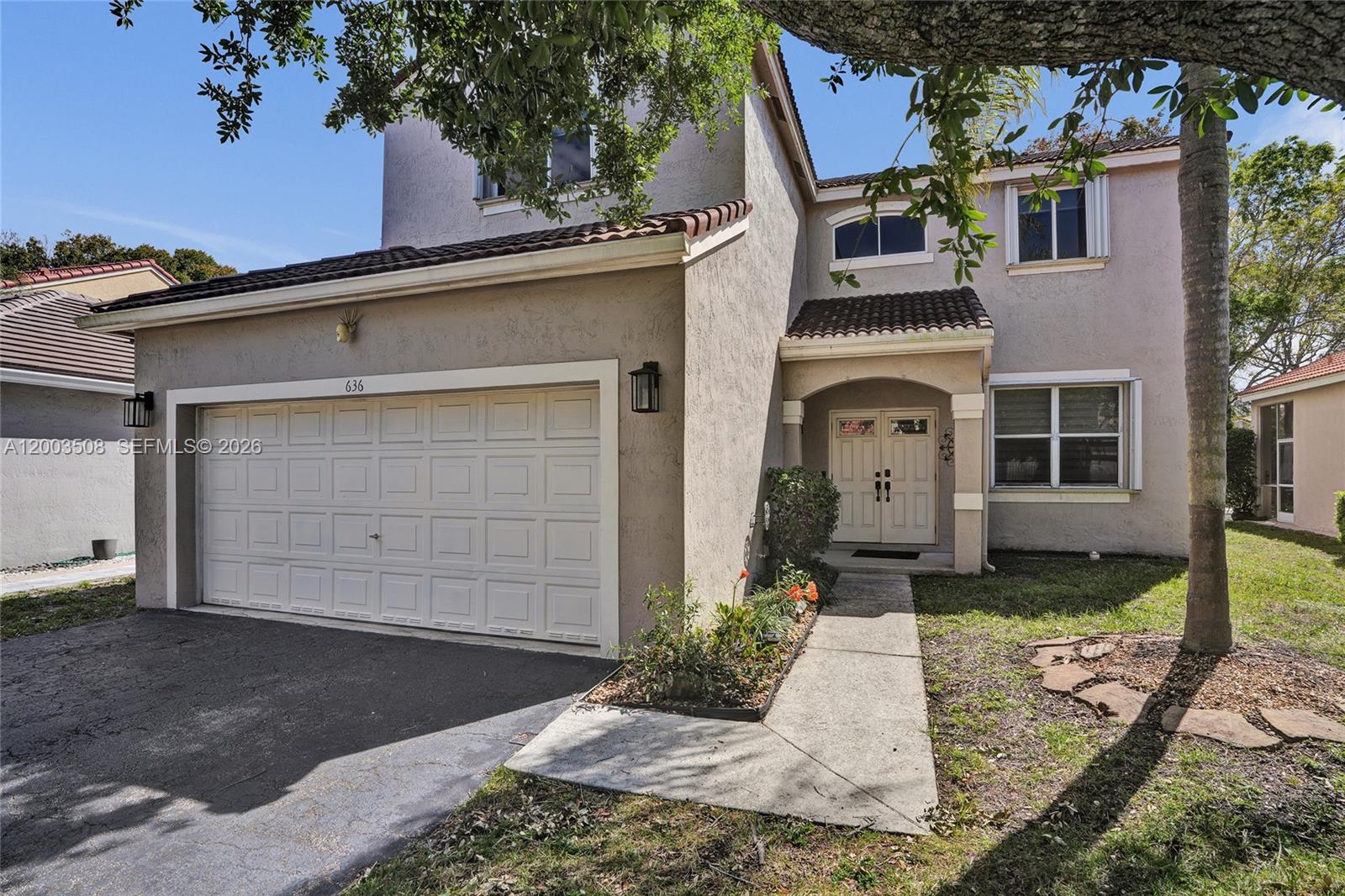 A two-story stucco house features a two-car garage, a tiled roof, and a front walkway — 636 Sand Creek Cir, Weston FL 33327, WESTON, FL