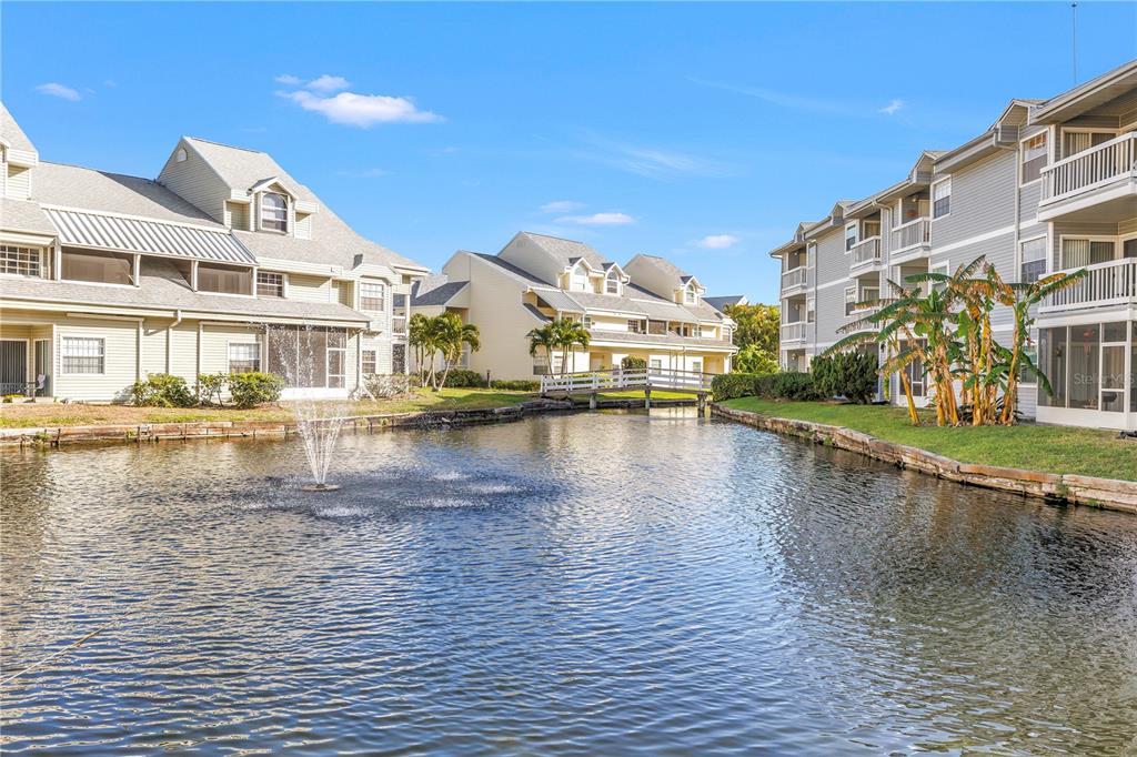 A pond with a fountain sits between two multi-story apartment buildings with a small bridge — 6939 STONES THROW CIRCLE N UNIT 6206, ST PETERSBURG, FL