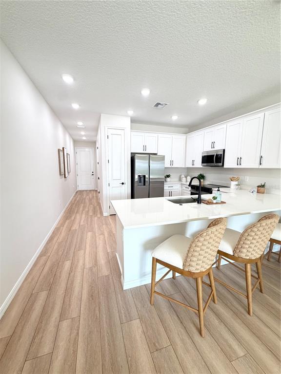 A hallway with light wood-look flooring leads to an open-concept living area and kitchen — 5837 ANGELA LEYLA PLACE, RIVERVIEW, FL