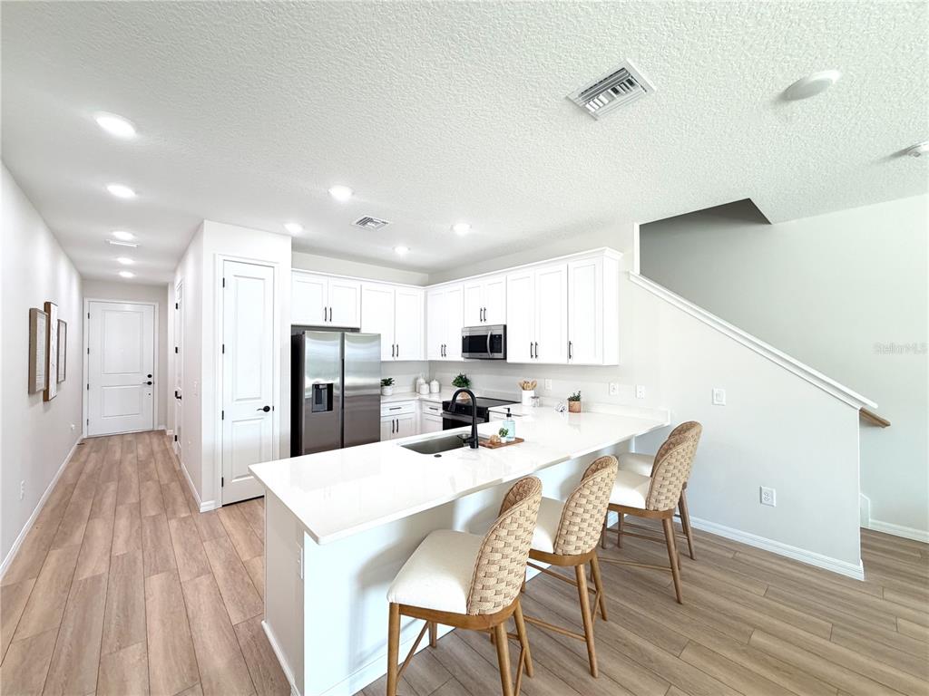 A modern kitchen features white cabinetry, a quartz island with bar stools, and wood flooring — 5837 ANGELA LEYLA PLACE, RIVERVIEW, FL