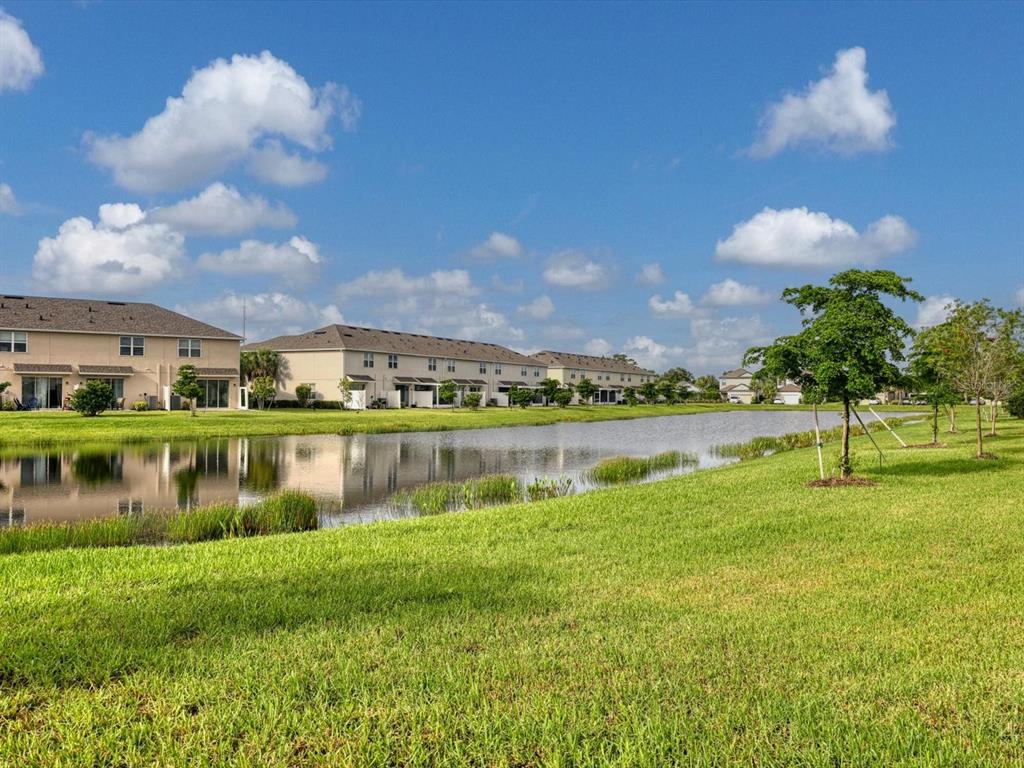 A pond sits in front of several multi-story residential buildings under a blue sky — 5739 ARCHIPELAGO STREET, NOKOMIS, FL