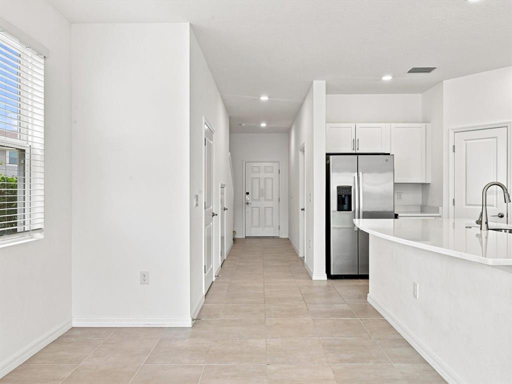 A bright kitchen and hallway feature white cabinets, stainless steel appliances, and light tile flooring — 5739 ARCHIPELAGO STREET, NOKOMIS, FL