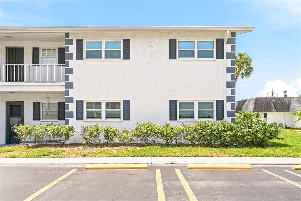A two-story apartment building exterior features white stucco walls, dark shutters, and a parking lot — 202 46TH AVENUE TERRACE W UNIT #209, BRADENTON, FL