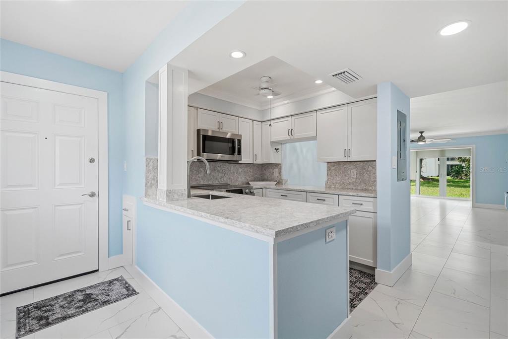 A kitchen with white cabinets, light countertops, and blue walls opens to a living area — 202 46TH AVENUE TERRACE W UNIT #209, BRADENTON, FL