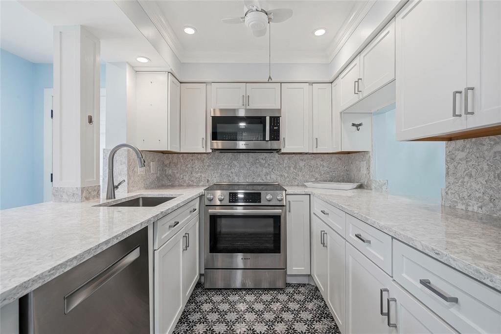 A kitchen features white cabinets, stainless steel appliances, marble-look countertops, and patterned floor tiles — 202 46TH AVENUE TERRACE W UNIT #209, BRADENTON, FL