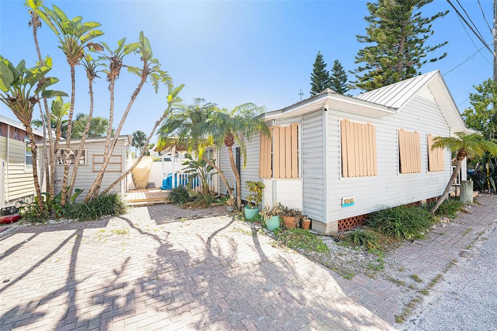 A light-gray house with hurricane shutters and a brick driveway surrounded by palm trees — 125 95TH AVENUE, TREASURE ISLAND, FL