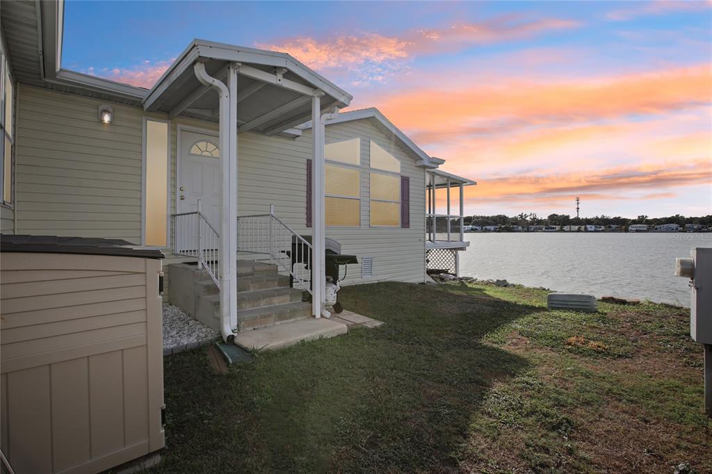 An exterior view of a light-colored house with a covered porch overlooking a lake — 8420 FANTASIA PARK WAY, RIVERVIEW, FL
