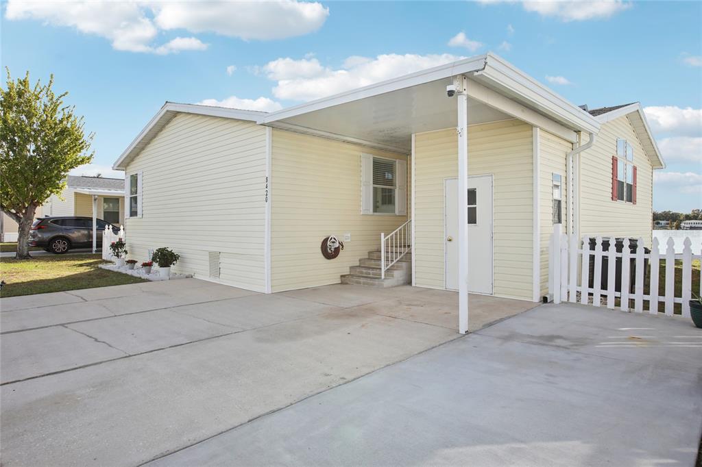 A light yellow manufactured home features a concrete driveway, a carport, and a white fence — 8420 FANTASIA PARK WAY, RIVERVIEW, FL
