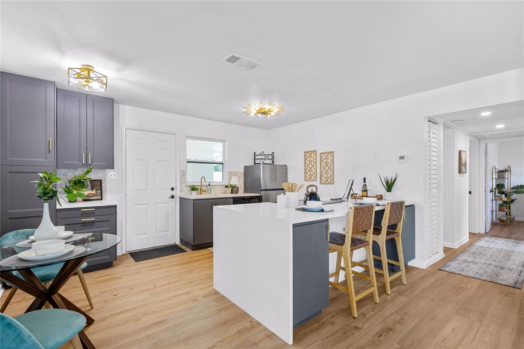 A kitchen features dark gray cabinets, a white quartz island, and light wood-look flooring — 4735 W WISCONSIN AVENUE, TAMPA, FL