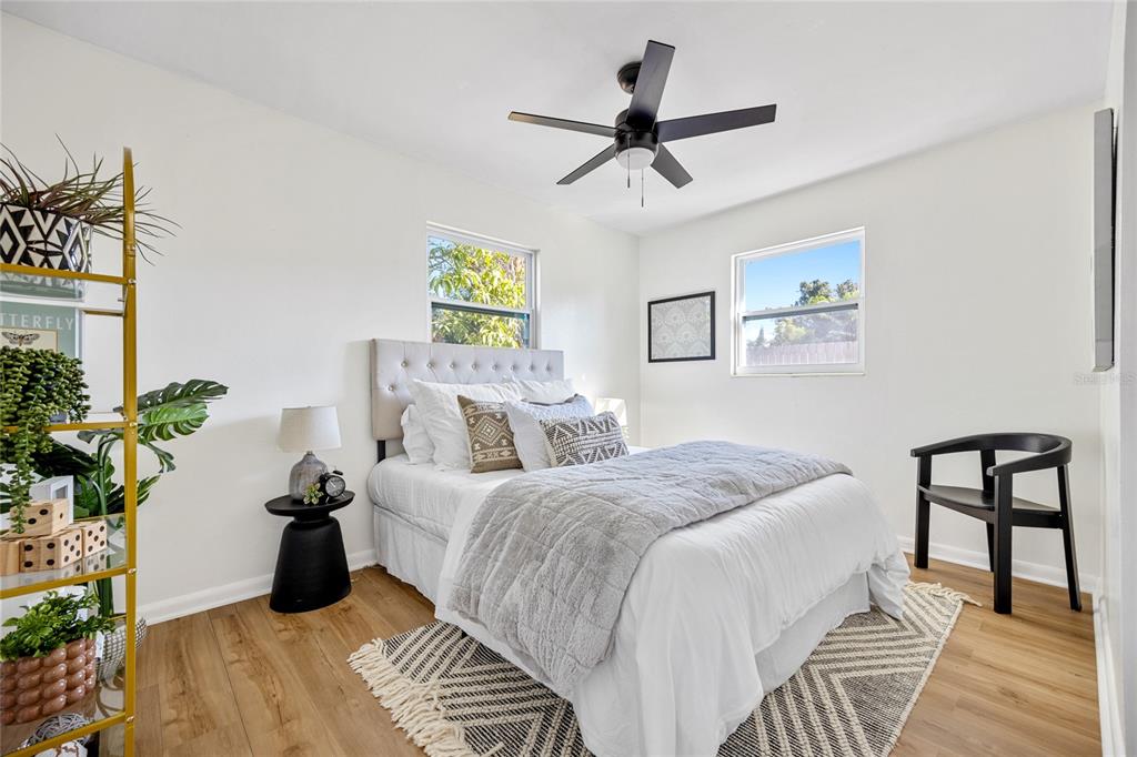 A bedroom features a bed with a tufted headboard, a ceiling fan, and wood-look flooring — 4735 W WISCONSIN AVENUE, TAMPA, FL