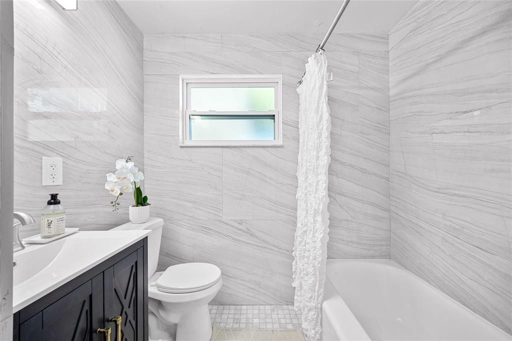 A modern bathroom features a white vanity, a toilet, and a bathtub with gray-veined tile walls — 4735 W WISCONSIN AVENUE, TAMPA, FL