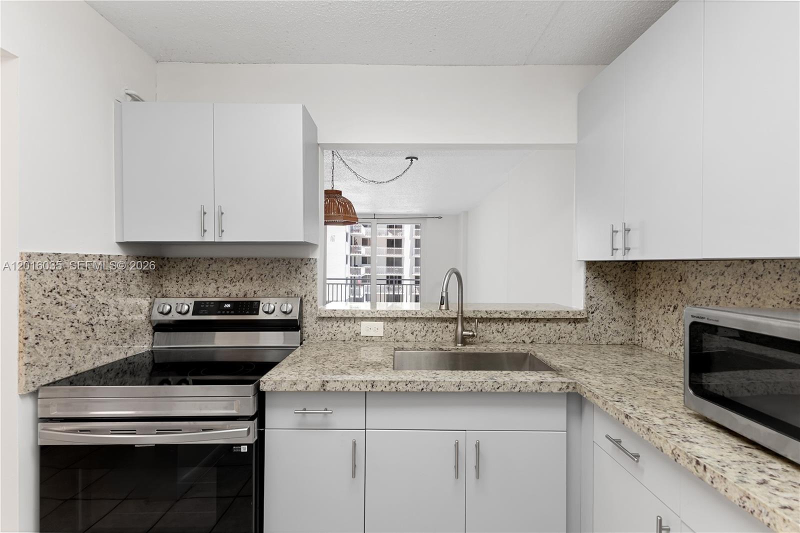 A kitchen features white cabinets, granite countertops, a stainless steel stove, and a pass-through window — 345 Ocean Dr # 424, Miami Beach FL 33139, MIAMI BEACH, FL