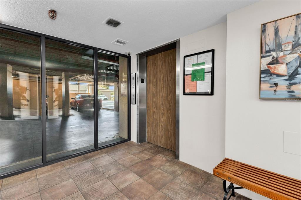An indoor lobby area features a wood-paneled elevator, a wooden bench, and glass-walled parking views — 3006 CARING WAY UNIT 615, PORT CHARLOTTE, FL
