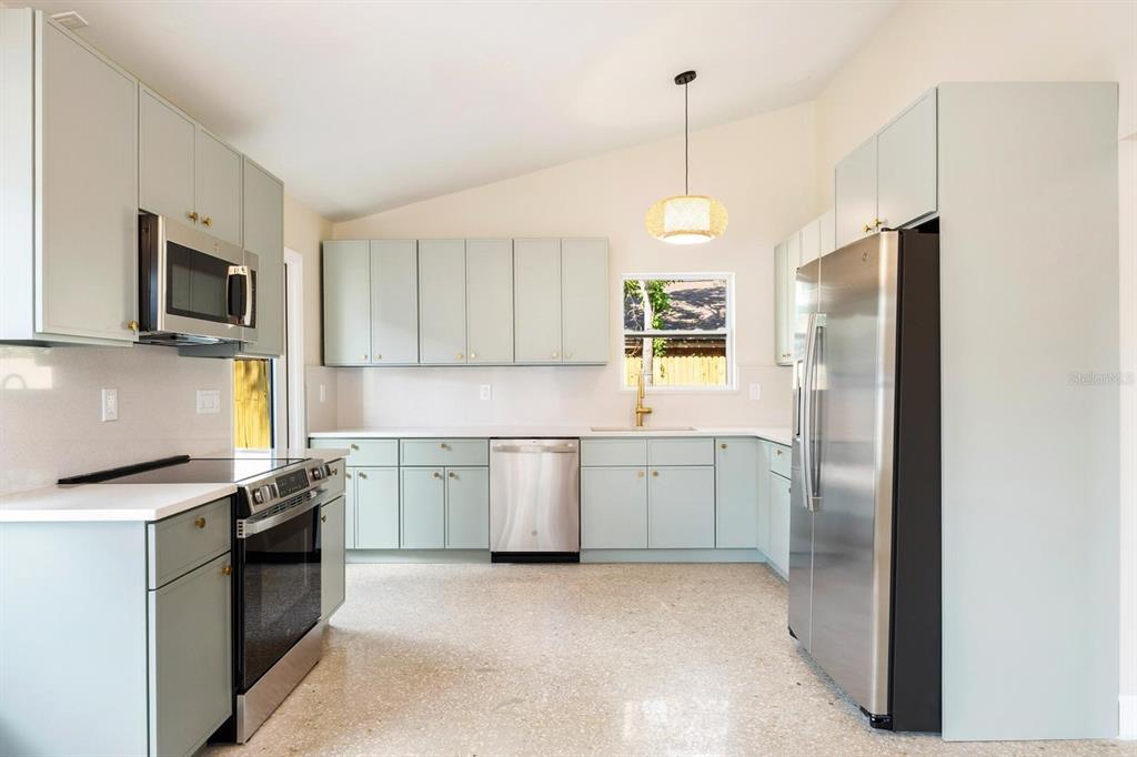 A kitchen features light green cabinets, stainless steel appliances, white countertops, and terrazzo flooring — 419 64TH AVENUE S, ST PETERSBURG, FL