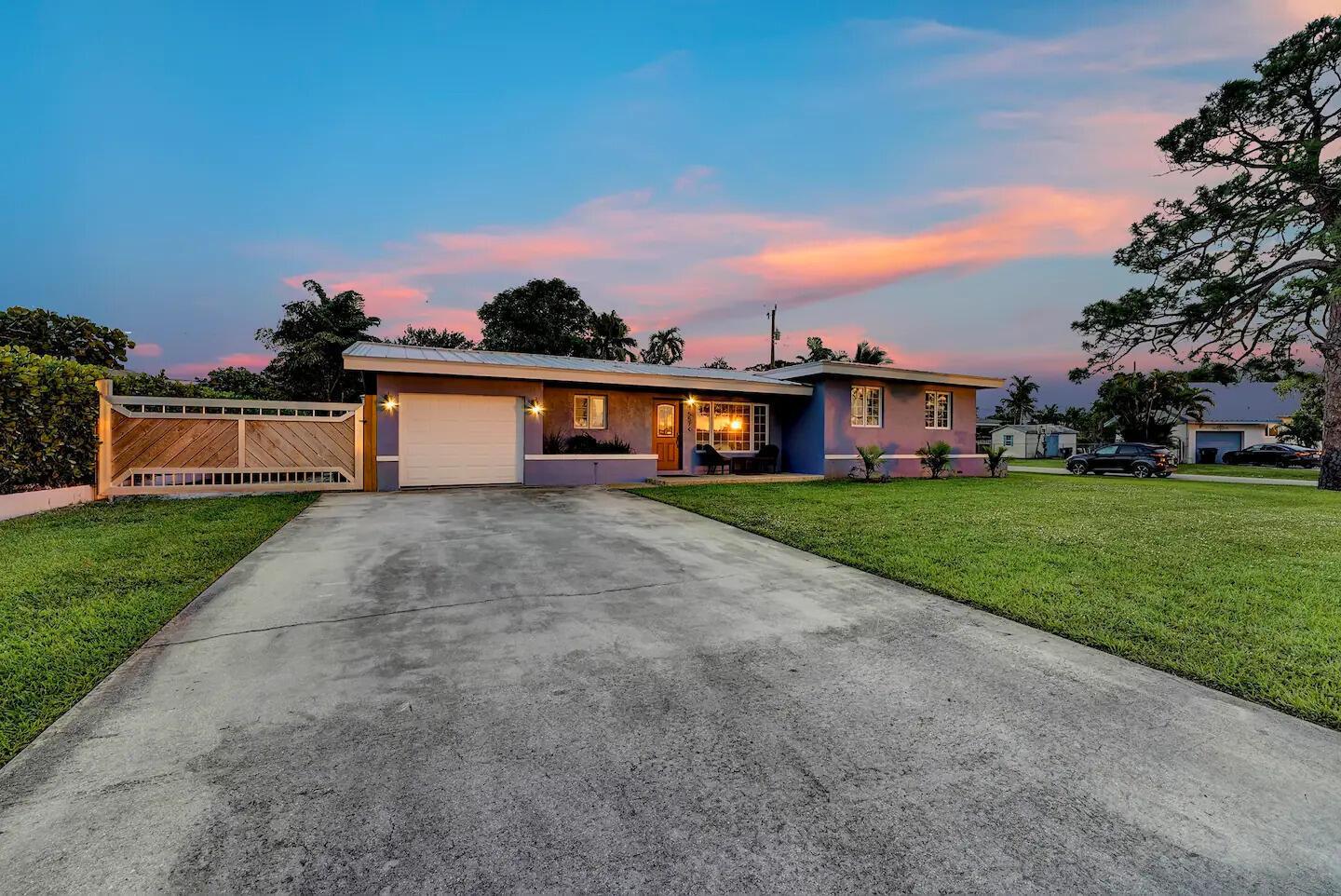 A single-story purple house with a white garage door and a concrete driveway at sunset — 5574 Lake Osborne Drive, Lake Worth FL 33461, LAKE WORTH, FL