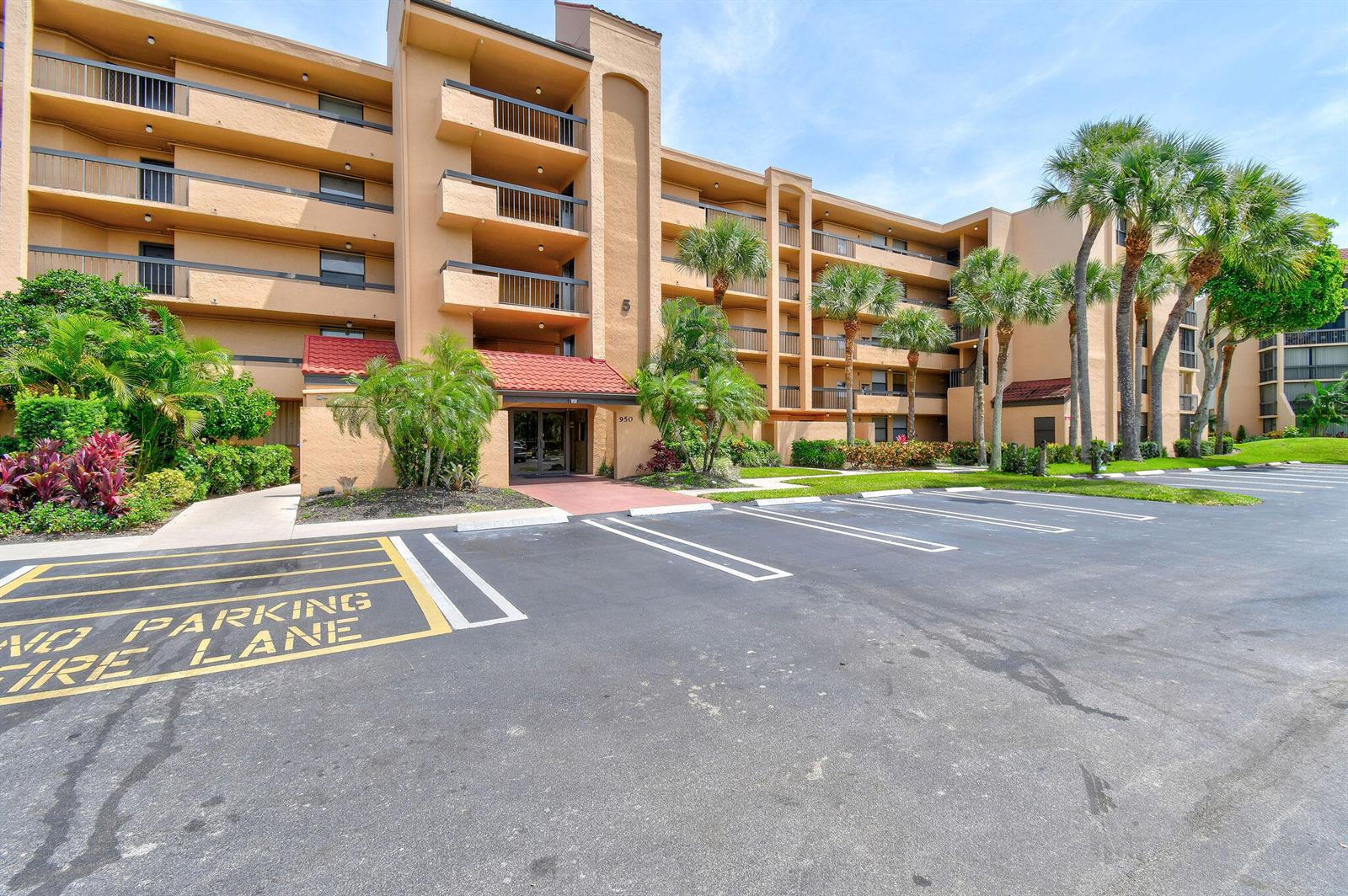 A multi-story tan apartment building features balconies and a parking lot in the foreground — 950 Egret Circle # 5108, Delray Beach FL 33444, DELRAY BEACH, FL
