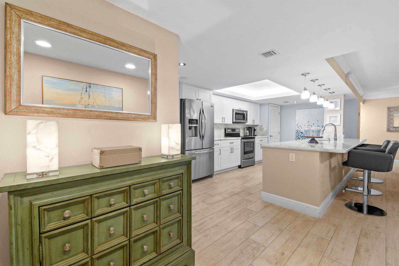 A kitchen with white cabinets and a breakfast bar overlooks a room with a dresser — 950 Egret Circle # 5108, Delray Beach FL 33444, DELRAY BEACH, FL