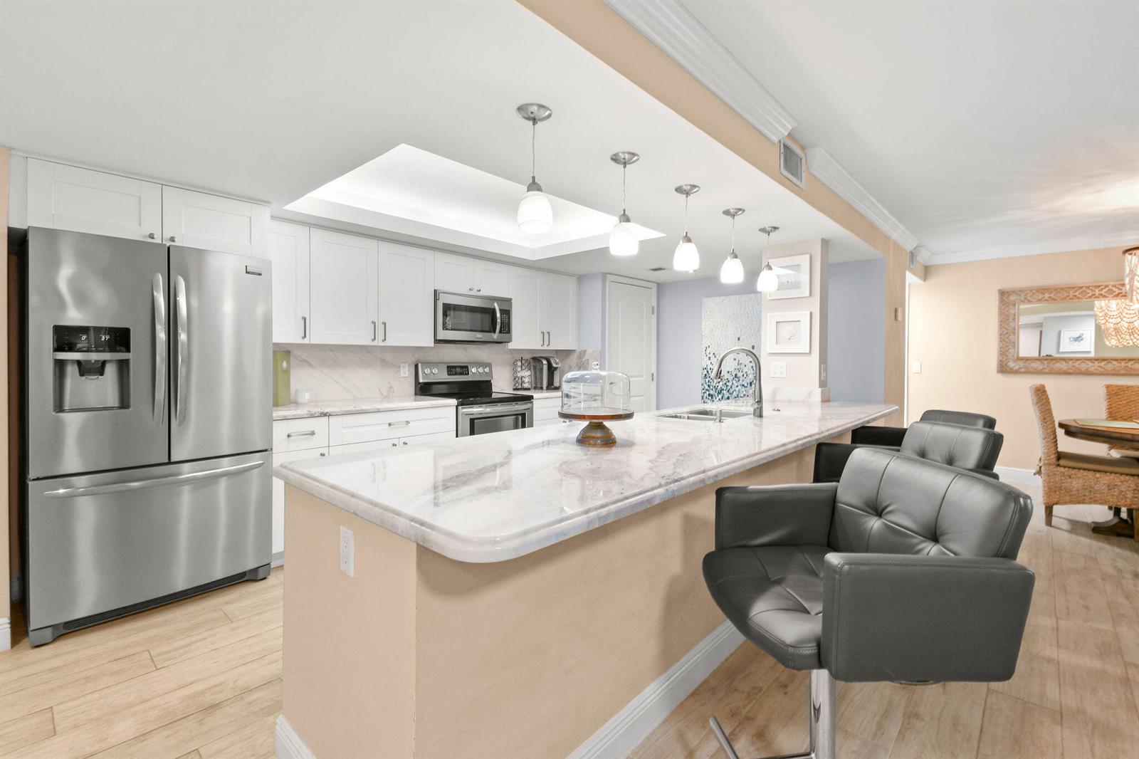 A kitchen features white cabinetry, stainless steel appliances, a marble-topped island, and gray bar stools — 950 Egret Circle # 5108, Delray Beach FL 33444, DELRAY BEACH, FL