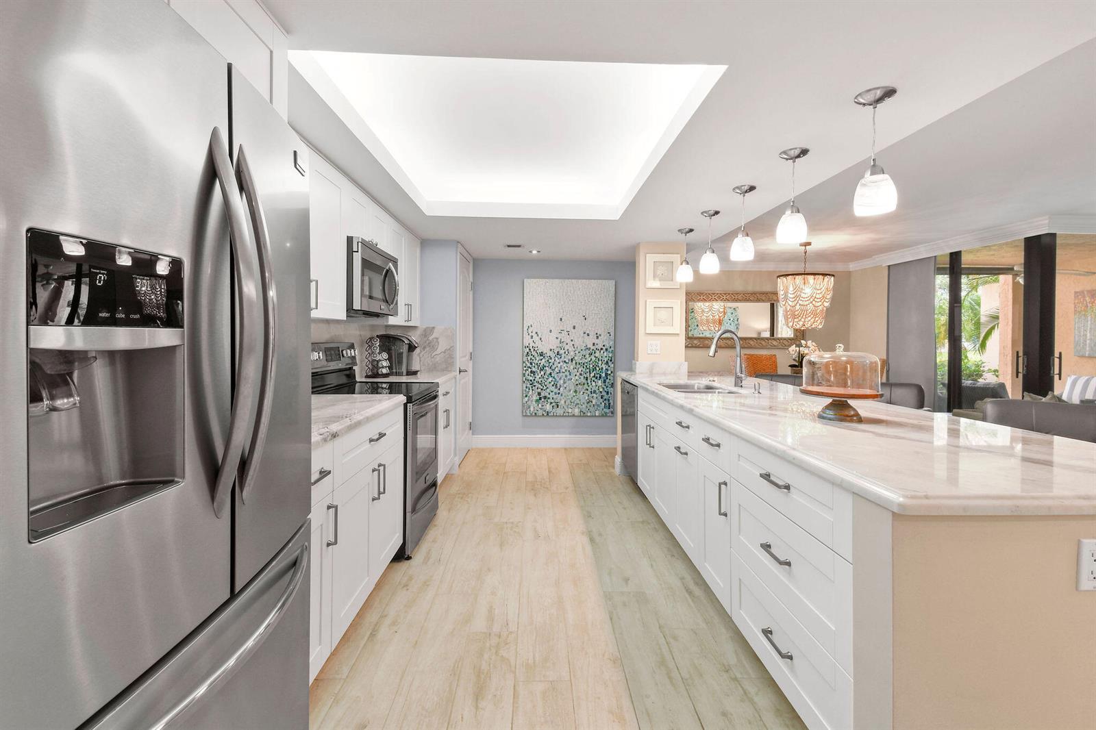 A modern kitchen features white cabinetry, a marble-topped island, stainless steel appliances, and wood-look flooring — 950 Egret Circle # 5108, Delray Beach FL 33444, DELRAY BEACH, FL