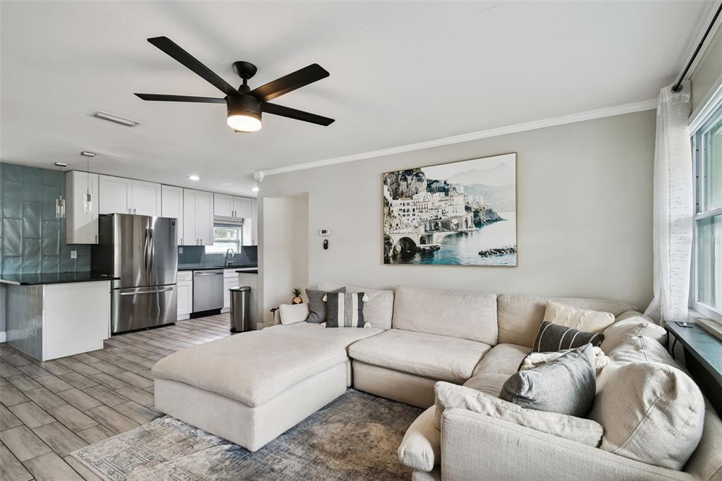 A living room with a sectional sofa and ceiling fan opens to a modern kitchen — 4722 W BAY AVENUE, TAMPA, FL
