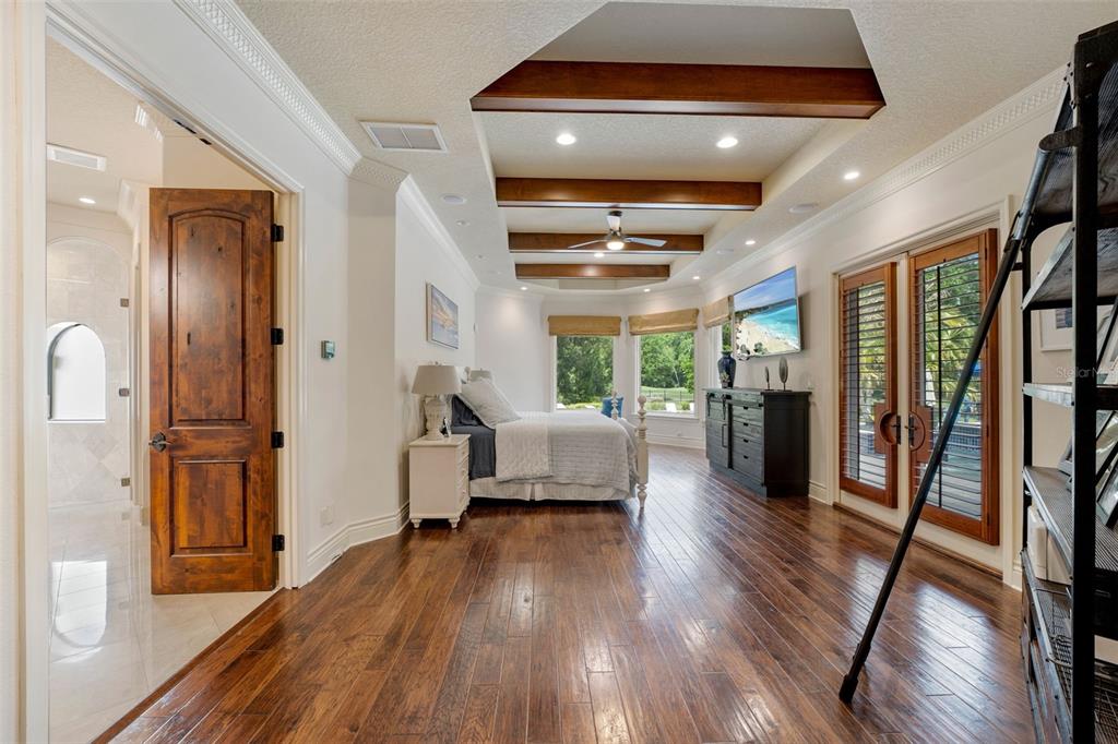 A bedroom with hardwood floors, a tray ceiling with wood beams, and glass patio doors — 6004 WINDHAM PLACE, TAMPA, FL