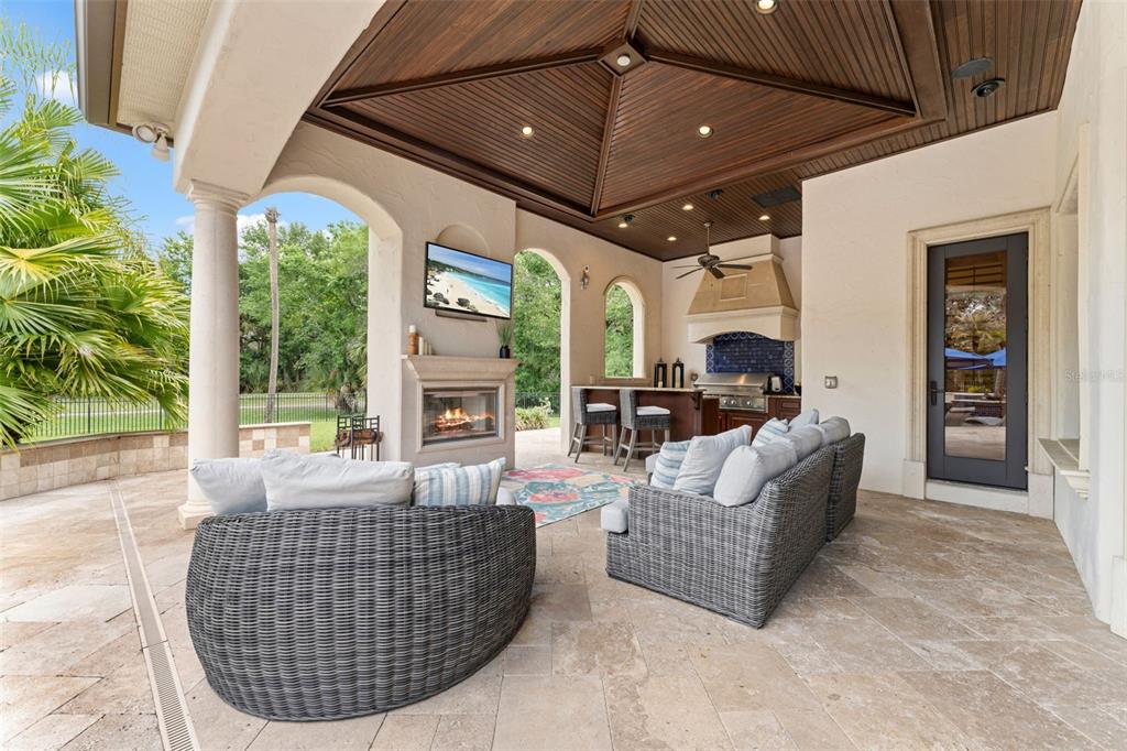 A covered outdoor patio features a fireplace, television, kitchen area, and wicker furniture — 6004 WINDHAM PLACE, TAMPA, FL