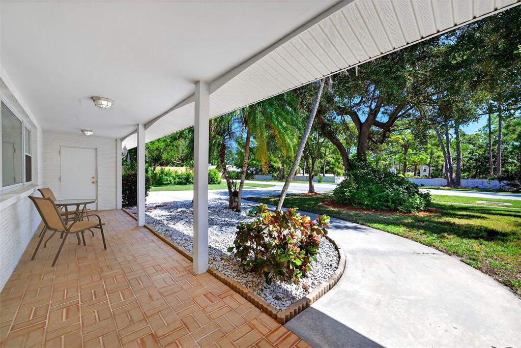 A covered brick patio features two chairs and overlooks a landscaped yard with trees — 4808 RIVERWOOD AVENUE, SARASOTA, FL