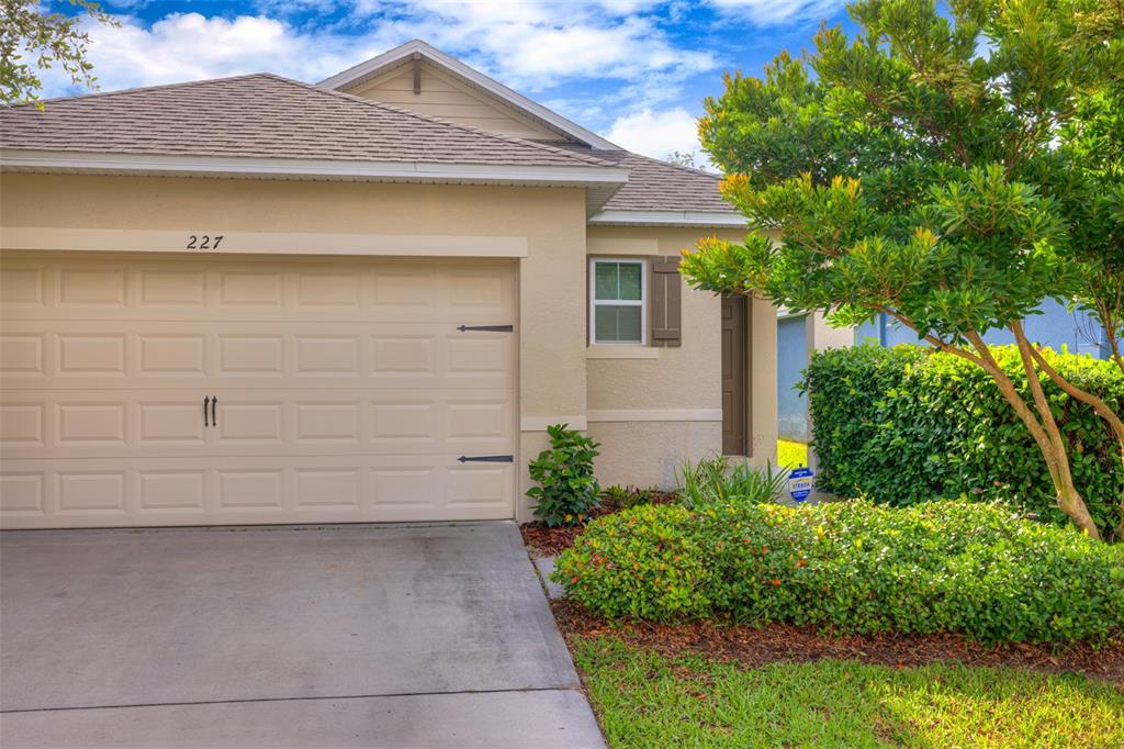 The exterior of a single-story house features a beige facade, a garage, and landscaping — 227 DUKE DRIVE, DELAND, FL