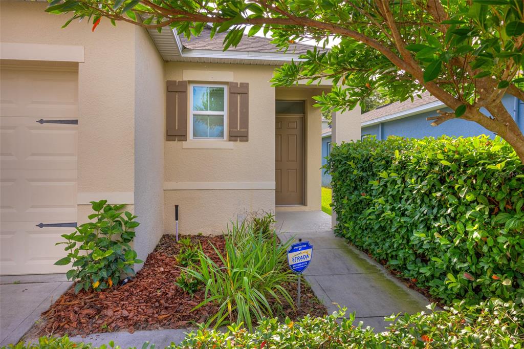 The exterior of a house features a tan stucco wall, a brown front door, and landscaping — 227 DUKE DRIVE, DELAND, FL
