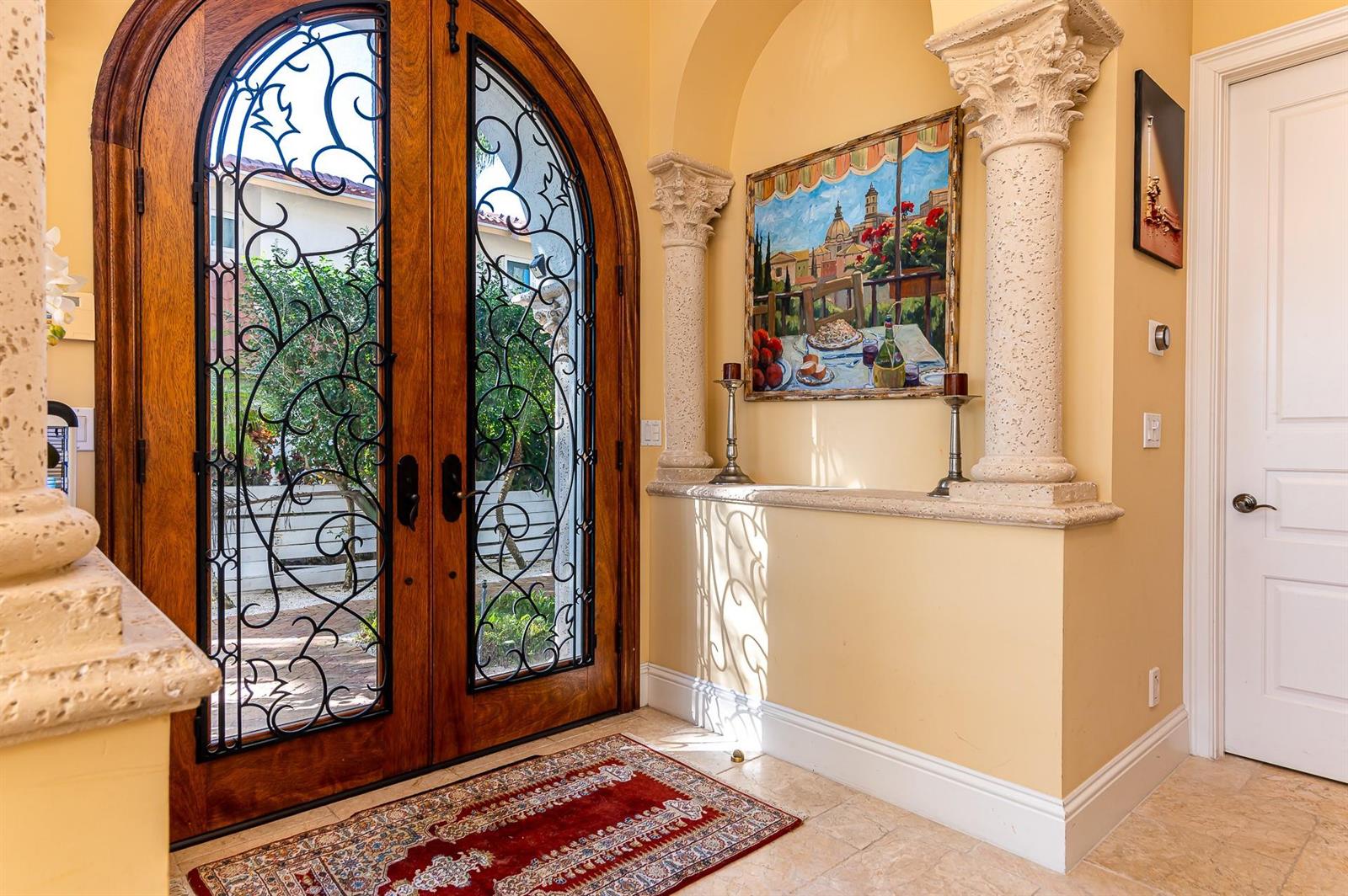 An entryway features arched wooden double doors with iron grilles, stone columns, and a painting — 580 Admirals Way, Delray Beach FL 33483, DELRAY BEACH, FL