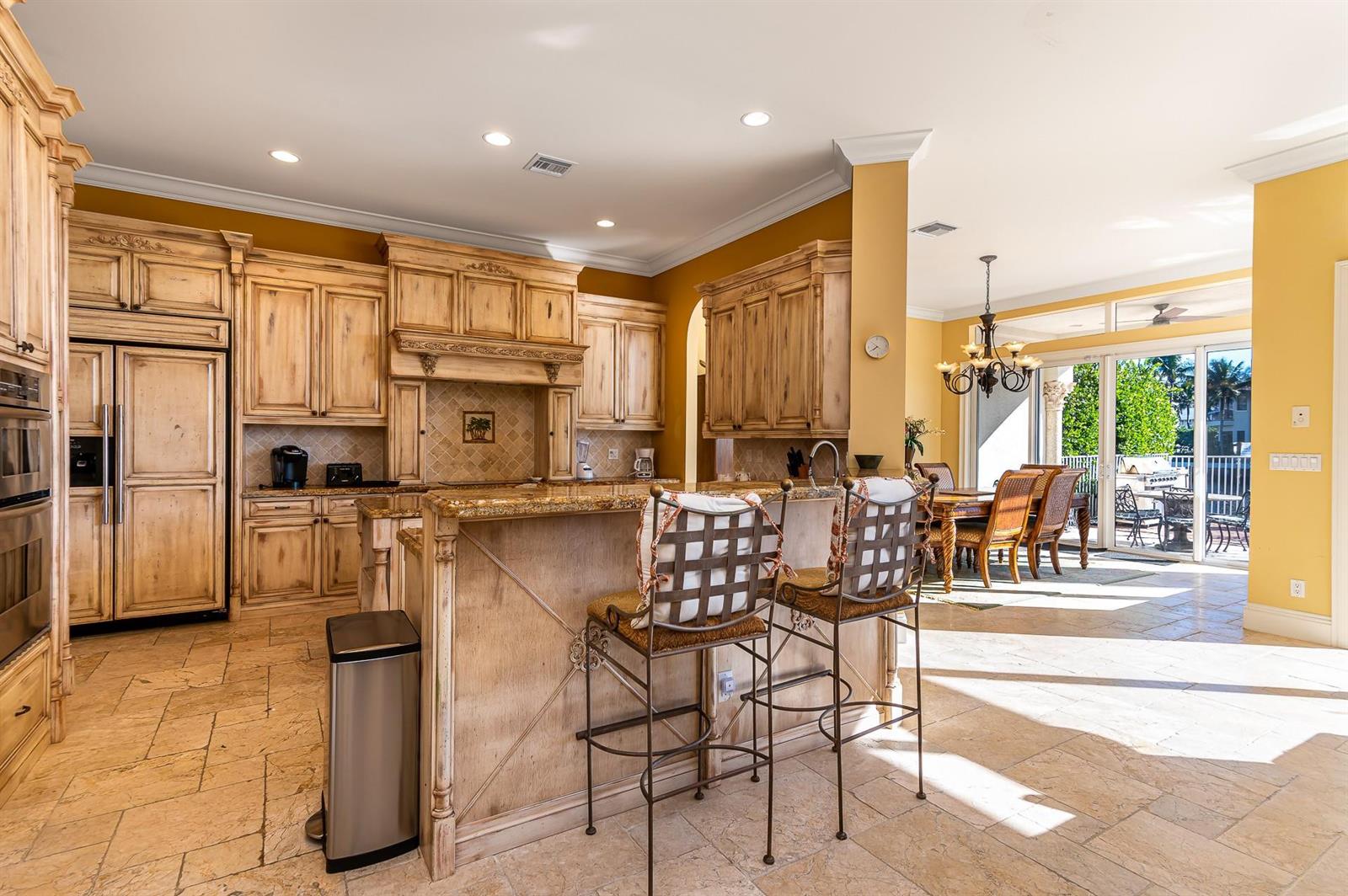 A kitchen with light wood cabinets, granite countertops, and a breakfast bar with two chairs — 580 Admirals Way, Delray Beach FL 33483, DELRAY BEACH, FL