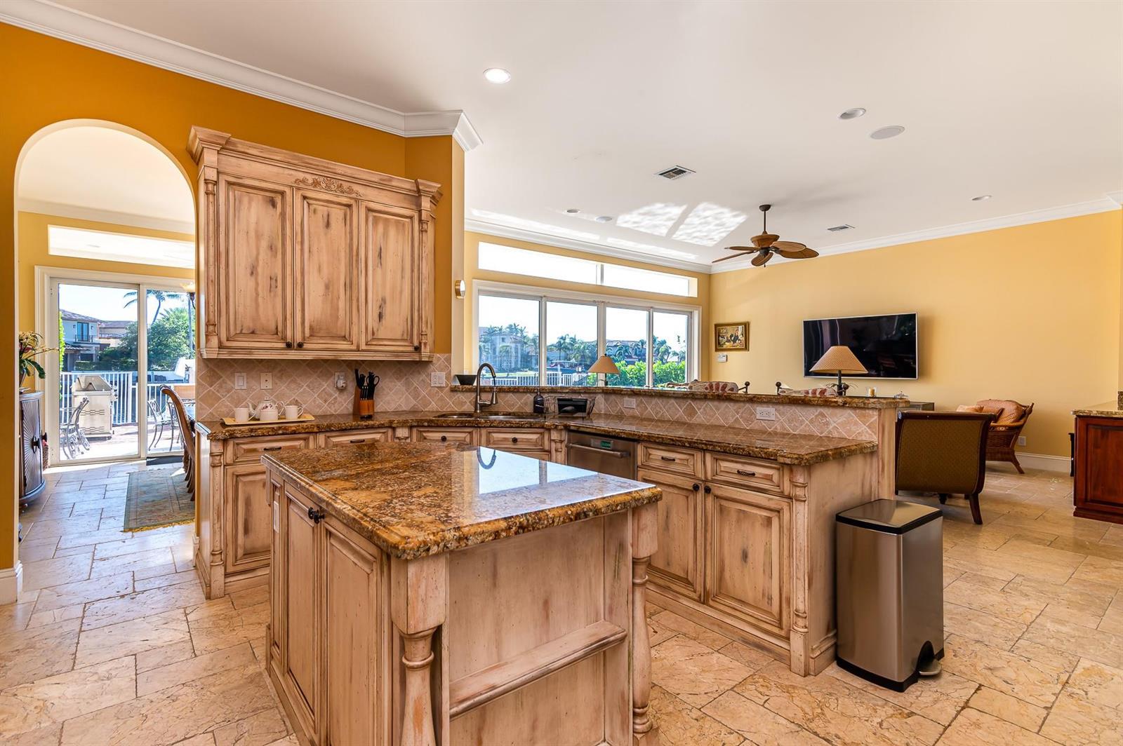 A kitchen with light-washed wood cabinets, granite countertops, and tile flooring, opening to a living area — 580 Admirals Way, Delray Beach FL 33483, DELRAY BEACH, FL